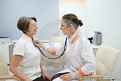 Female therapist listens to the chest of an elderly patient Stock Photo