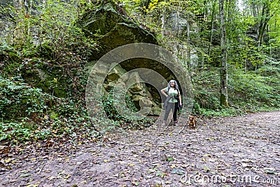 Female tourist hiker with her brown dachshund on a path taking a break next to a huge moss covered sandstone rock Stock Photo