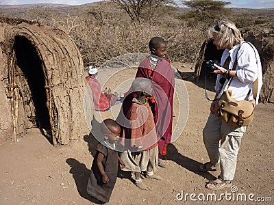 Female tourist talks to Masai children near village mud huts, Tanzania Editorial Stock Photo