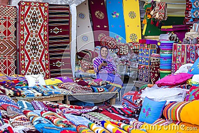 Female trader at Souq Waqif market in Doha, with multicolour carpets, kilims and other items. Doha, Qatar Editorial Stock Photo