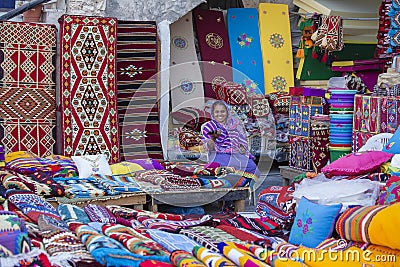 Female trader at Souq Waqif market in Doha, with multicolour carpets, kilims and other items. Doha, Qatar Editorial Stock Photo