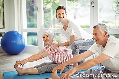 Female trainer assisting senior couple in performing exercise Stock Photo