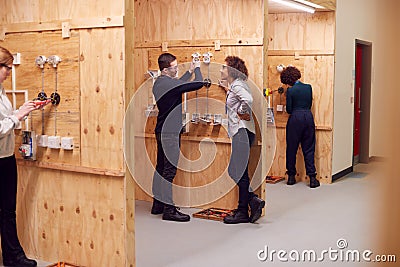 Female Tutor With Trainee Electricians In Workshop Studying For Apprenticeship At College Stock Photo