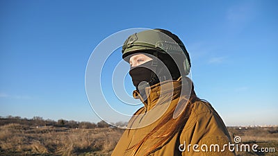 Female ukrainian army soldier walking at the field. Woman in military uniform and helmet going on meadow at sunset Stock Photo