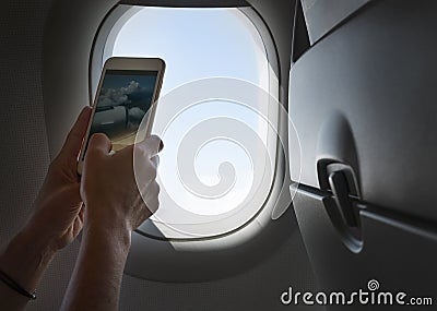 Female using her smartphone for photographing clouds and aircraft engine through the porthole. Active traveling and flying by Stock Photo