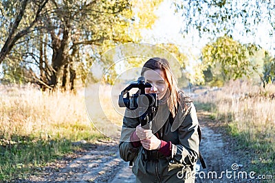 Female videographer holding a gimbal with mirrorless camera. Woman with stabilized camera rig filming outdoors on a sunny Stock Photo