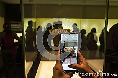 Female visitor taking a picture with a smartphone to an ancient golden piece Editorial Stock Photo