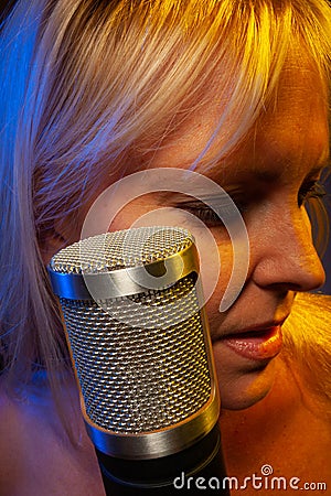 Female vocalist under gelled lighting with condenser microphone Stock Photo