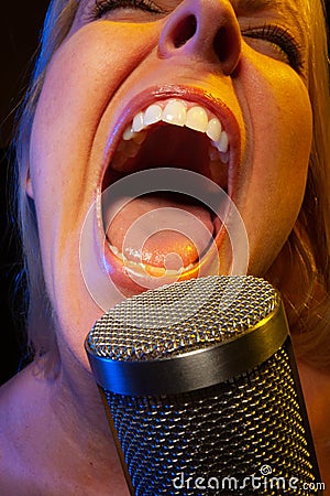 Big mouthed female vocalist under gelled lighting sings with passion into condenser microphone Stock Photo