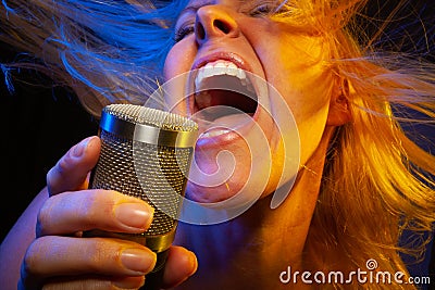 Spinning female vocalist under gelled lighting sings with passion into condenser microphone Stock Photo