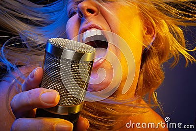 Entertaining female vocalist under gelled lighting sings with passion into condenser microphone Stock Photo