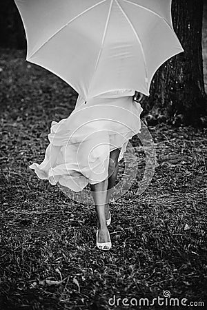 Female in a white dress holding a white umbrella in front of her while walking in the forest Stock Photo