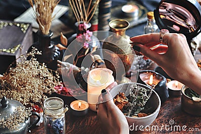 Female wiccan witch holding grey clay pot in her hands preparing ingredients for a spell at her altar Stock Photo