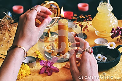 Female wiccan witch wearing vintage jewelry lighting a yellow candle on her Litha midsummer Sabbat Solstice celebration altar Stock Photo