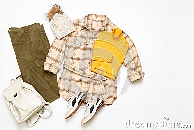 Female winter or autumn stylish clothing set. Plaid checkered shirt, yellow sweater, green corduroy trousers, hat with pompom, Stock Photo