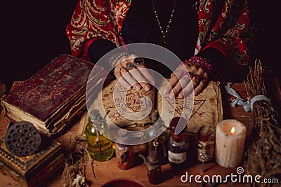 Female witch making potion on dark background, magic bottles with potions and candles on table of alchemist, Halloween theme Stock Photo