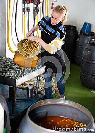 Female worker fills glass jars with olives for canning Stock Photo