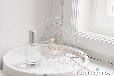 Feminine cosmetic still life scene. Glass bottle, flacon with perfume or eau de toilette and dry grass on white marble Stock Photo