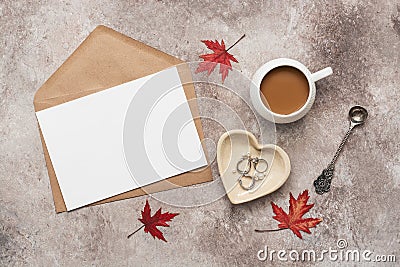 Feminine desktop, home office. Blank card, craft envelope, a cup of coffee with milk and jewelry. Beige grunge background. Modern Stock Photo