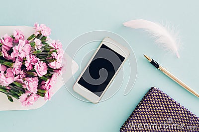 Feminine flat lay on blue background, top view of woman`s desktop with envelope, flowers, pen, notepad and smartpho Stock Photo