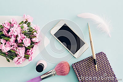 Feminine flat lay on blue background, top view of woman`s desktop with envelope, flowers, pen, notepad and smartpho Stock Photo