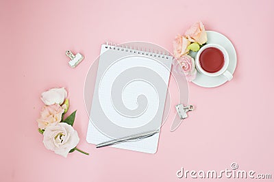 Feminine home office workspace. Notebook with copyspace. Flat lay, social media. Pink flowers and tea on pastel pink background. Stock Photo