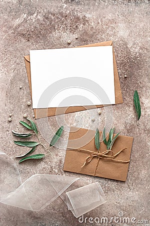 Feminine wedding invitation mockup. Blank card, craft envelope, olive branch and silk ribbon. Beige grunge background. Top view, Stock Photo