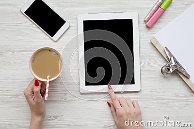 Feminine work space with tablet, noticepad, sheet, latte ice, smartphone and female hands over white wooden background, top view. Stock Photo