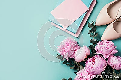 Feminine workspace with notebook, shoes, pink peony, eucalyptus flower on blue background. Top view, copy space. Blogger, feminine Stock Photo