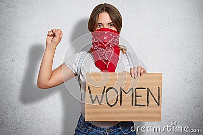 Feminism concept. Self confident young woman feminist protects womens rights, takes part in protest, keeps hands in fist raised, w Stock Photo