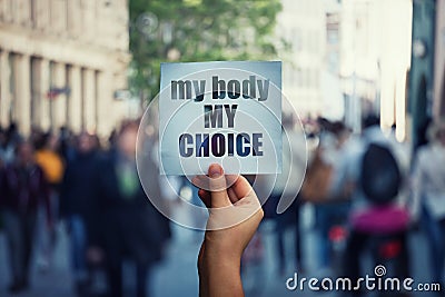 Feminist hands holding a protest banner with the message my body my choice over a crowded street. Human rights concept against Stock Photo