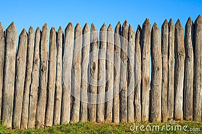 Fence made of sharp wooden stakes against the blue sky. Wooden fence vertical logs pointed against the sky protection against Stock Photo