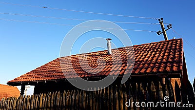 Fence made of sharp wooden stakes. Wooden houses with red tiled roof and blue clear sky. Sunny day Stock Photo