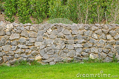 Fence real stone wall surface with cement on green grass field Stock Photo