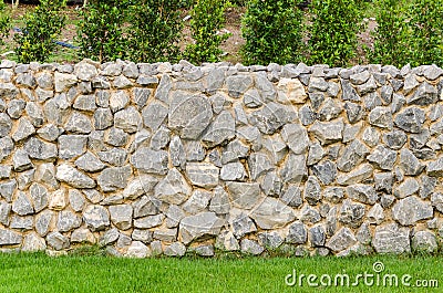 Fence real stone wall surface with cement on green grass field Stock Photo