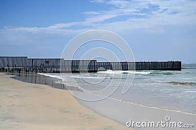 A fence on the United States - Mexico border where it meets the Pacific Ocean in Border Field State Park Beach Stock Photo