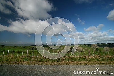 Scenic rural landscape of pastureland with wood posts and wired fence, blue sky and dramatic clouds in Waitomo, New Zealand Stock Photo