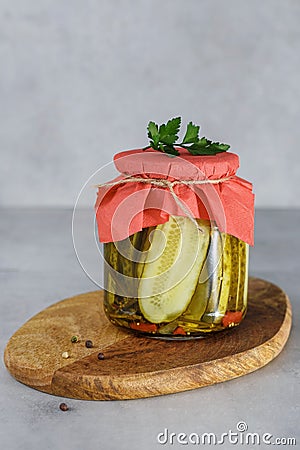 Fermented preserved cucumber in glass jar on wooden stay. Stock Photo