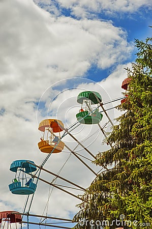 Ferris wheel in the city Park. green tree, spruce and blue sky with white clouds. Editorial Stock Photo