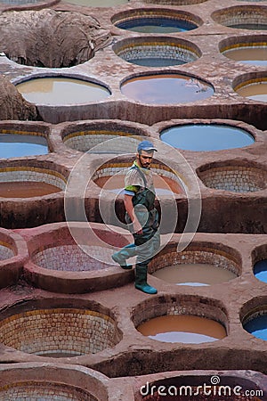 Fes, Morocco - male worker walks across stone vessels with colored dyes at Chouara Tannery in Fes el Bali. Editorial Stock Photo