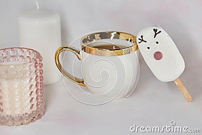 Festive afternoon tea with white cup, cute marshmallow deer, gingerbread cookie and pink candle. Aesthetic tea time Stock Photo