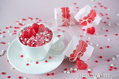 Coffee cup, full of multicolor sweet sprinkles sugar candy hearts and packing Valentine`s Day gifts. Love and Valentine`s day Stock Photo