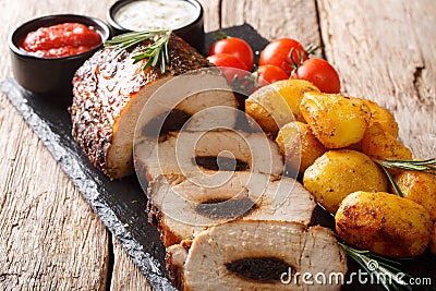 Festive baked pork stuffed with prunes with new potatoes and sauces close-up. horizontal Stock Photo