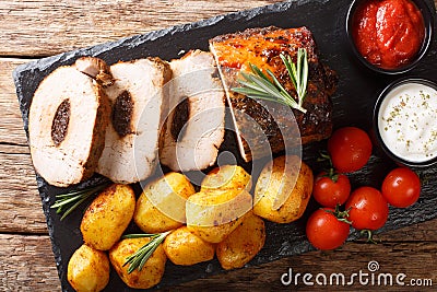 Festive baked pork stuffed with prunes with new potatoes and sauces close-up. Horizontal top view Stock Photo
