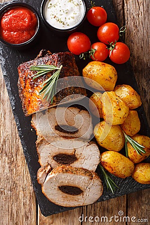 Festive baked pork stuffed with prunes with new potatoes and sauces close-up. Vertical top view Stock Photo