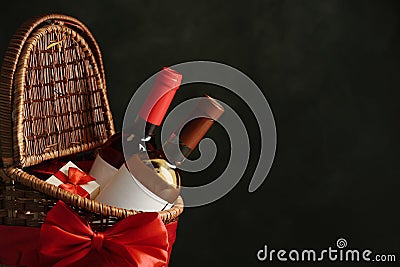 Festive basket with bottles of wine and gift against dark background Stock Photo