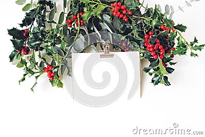 Festive Christmas mockup scene. Greeting card with golden paper binder clip, eucalyptus and holly red berries, leaves Stock Photo