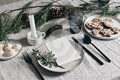 Festive Christmas table setting. Black cutlery, pine tree branch decoration. Gingerbread cookies, candleholder and glass Stock Photo