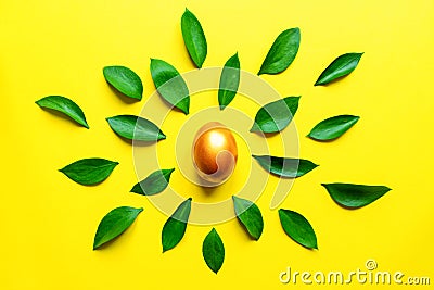 Festive easter background. Golden, stylish pinted egg with ruskus leaves on yellow background Stock Photo