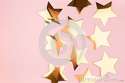 Festive gold glossy stars on pastel pink background, top view, border. Stock Photo